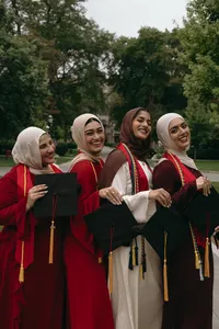 Four individuals smiling and looking away from camera, all holding graduation caps and wearing graduation sashes