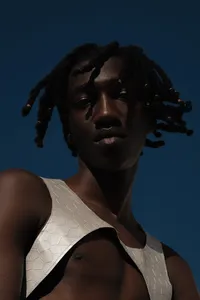 Close up of human wearing white garment with a deep navy blue background looking down at camera