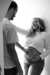 Black and white image of two humans, with one with a cropped white shirt, with one touching the other one's baby bump.