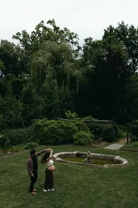 Two humans walking in greenery area and dancing while one shows off baby bump