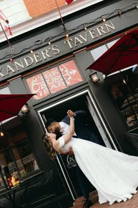 Two individuals kissing and holding hands while the one in a bridal gown is being dipped in front of doorway