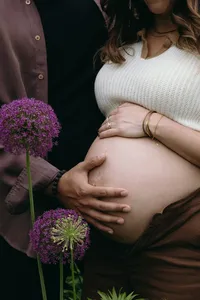 Human touching hand on their bare baby bump while florals surround them