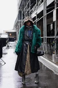 Human walking outdoors with a teal green fluffy coat and a brown bucket hat