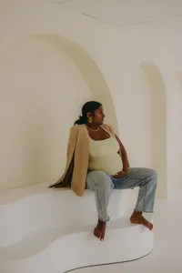 Pregnant human in yellow shirt with brown sweater, looking away from camera while holding baby bump