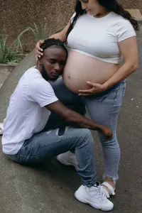 Two humans in jeans and white shirts, while one rests their head on the bare baby bump of the other