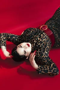 Individual laying down with leopard outfit on, with red nails, red lipstick and a bold red background