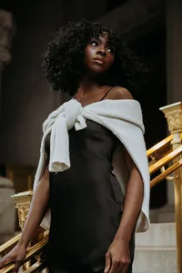 Human with black dress, white sweater tied around their chest, looking away from the camera