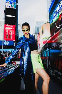 Human in the city wearing neon green skirt, blue trench coat and sunglasses