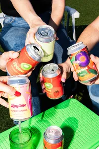 Multiple hands holding five cans of brightly colored Anytime drinks