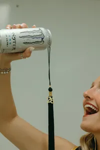 Human holding up Monster energy drink with a graduation tassel and '26 on it