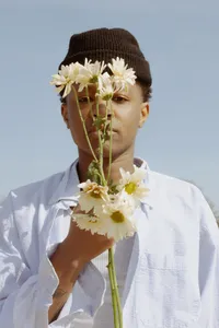 Close up of human with white shirt, holding a few flowers, with blue background