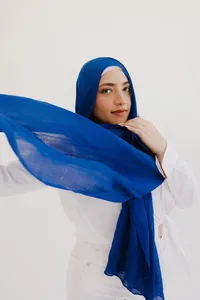 Human with white outfit and cobalt blue head scarf looking at the camera