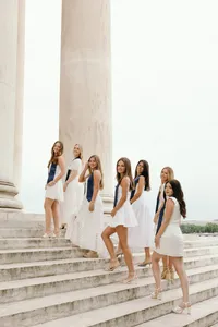 Group of seven humans, all dressed in white, looking at the camera and walking up the steps of building