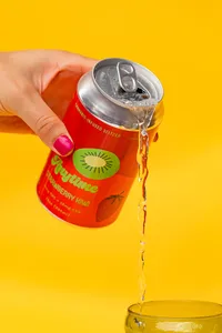Hand holding Anytime kiwi drink and pouring it out with a yellow background