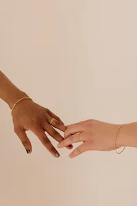 Two hands extended and touching one another at the fingertip with matching wedding rings and gold bracelets