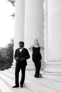 Black and white image of two humans dressed in black outside of beautiful polished building