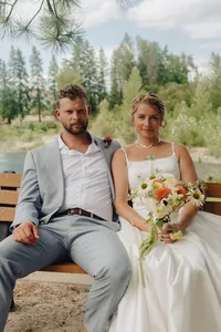 A portrait of a couple sitting on a bench holding bouquet of flowers.