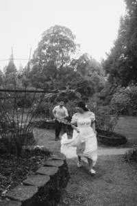 An engaged couple chasing each other at a rose garden.