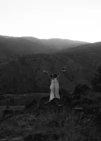 an extreme wide shot of a married couple holding their bouquets in the air as they kiss behind the sunset.
