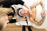 Overhead view of a woman receiving a facial treatment with a handheld device while lying on a treatment bed with her eyes closed.