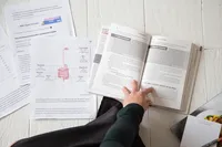 Overhead view of a person pointing to text in an open textbook beside study notes and a digestive system diagram.