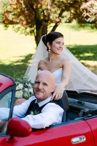 Newlyweds with their wedding bouquet beside the red vintage car