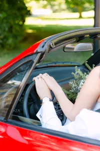 Bride’s hand resting on the steering wheel of a red vintage car