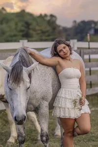 senior Girl in white dress leaning on her horse in a field near a feance