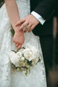 Bride and groom holding hands showing wedding rings, bouquet of white flowers below