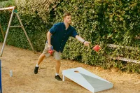 Guest playing cornhole on the lawn at a garden party wedding at Kites Barn, 35mm film