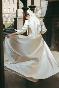 Bride holding the train of her wedding gown outside a historic stone building