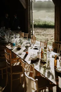 Long wedding reception table in a barn set with glassware and candles at golden hour