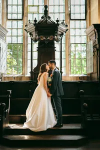 Couple kissing in a hall with tall leaded windows and wooden pews