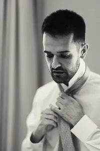 Black and white portrait of a groom in a waistcoat adjusting his shirt collar