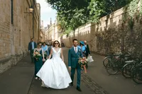 Bride and groom walking along a narrow Oxford lane with their wedding party behind them