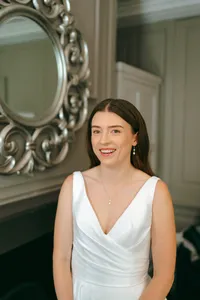 Smiling bride in a white V-neck gown in front of an ornate silver mirror