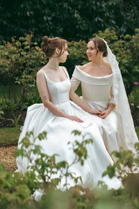 Two brides in wedding dresses sitting together in a garden, same-sex wedding photography