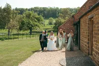 Wide shot of bride and groom walking hand in hand along a path with a barn in the distance