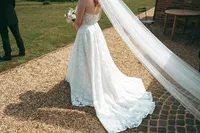 Bride walking along a gravel path, her long veil trailing behind her.