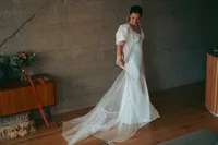 Bride in a flowing wedding dress with a sheer train, standing in a styled room