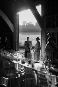 Wedding guests silhouetted at the reception table inside a barn overlooking the countryside