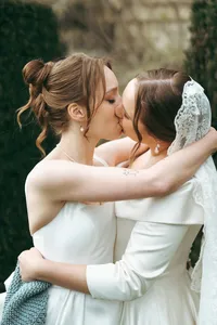 Close-up of two brides embracing and sharing a kiss, one wearing a lace veil