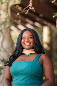 Smiling graduate in a green dress and graduation hood outdoors