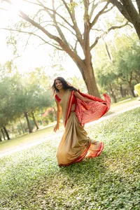 Woman in a red and beige sari moving through sunlit greenery