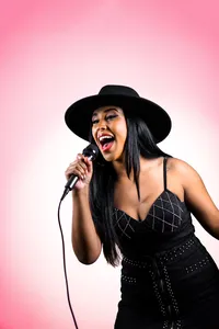 Singer performing into a microphone against a pink studio backdrop