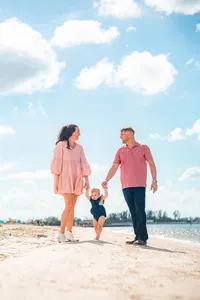 Parents walking on a sandy beach while holding their toddler's hands