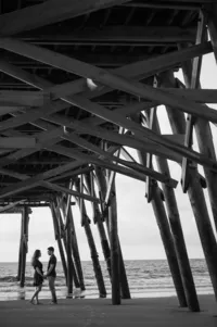 Couple under Garden City Pier during a Myrtle Beach SC engagement session photographed by Amberlee Christey.