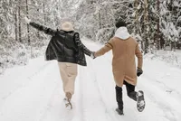 Couple seen from behind holding hands while walking through a snowy winter landscape