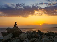 woman-meditating-on-top-of-a-boulder-in-front-of-sea-12314727