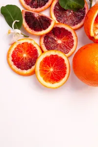 Sliced blood oranges and whole oranges on a white countertop